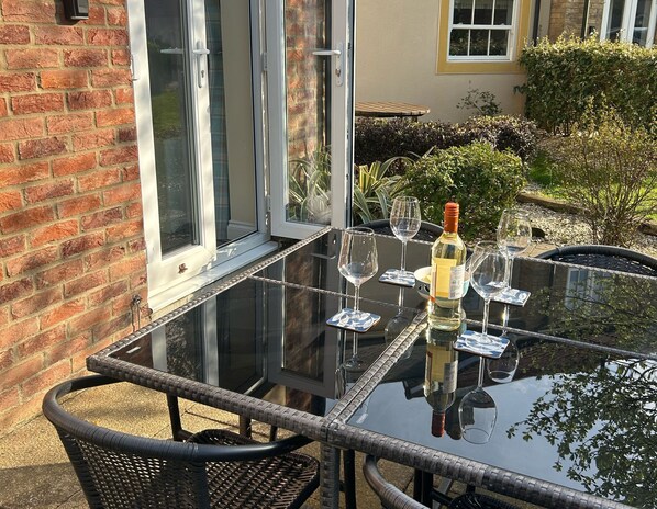A glass-top table with wine glasses and a bottle, surrounded by wicker chairs. - Seaside Cottage - a cottage that sleeps 4 guests in 2 bedrooms (Filey)