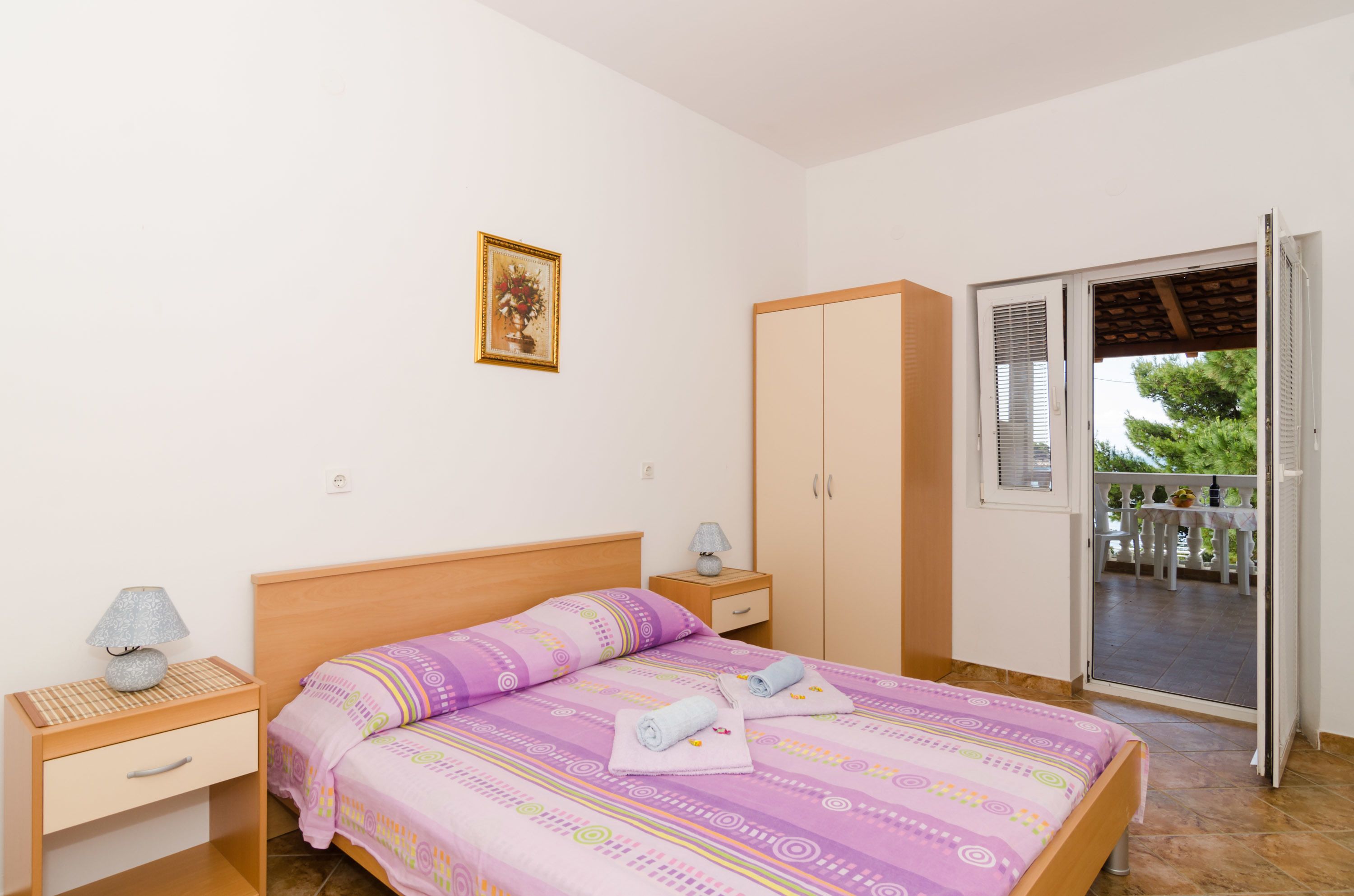 A bedroom with a bed, nightstands, a wardrobe, and a balcony.