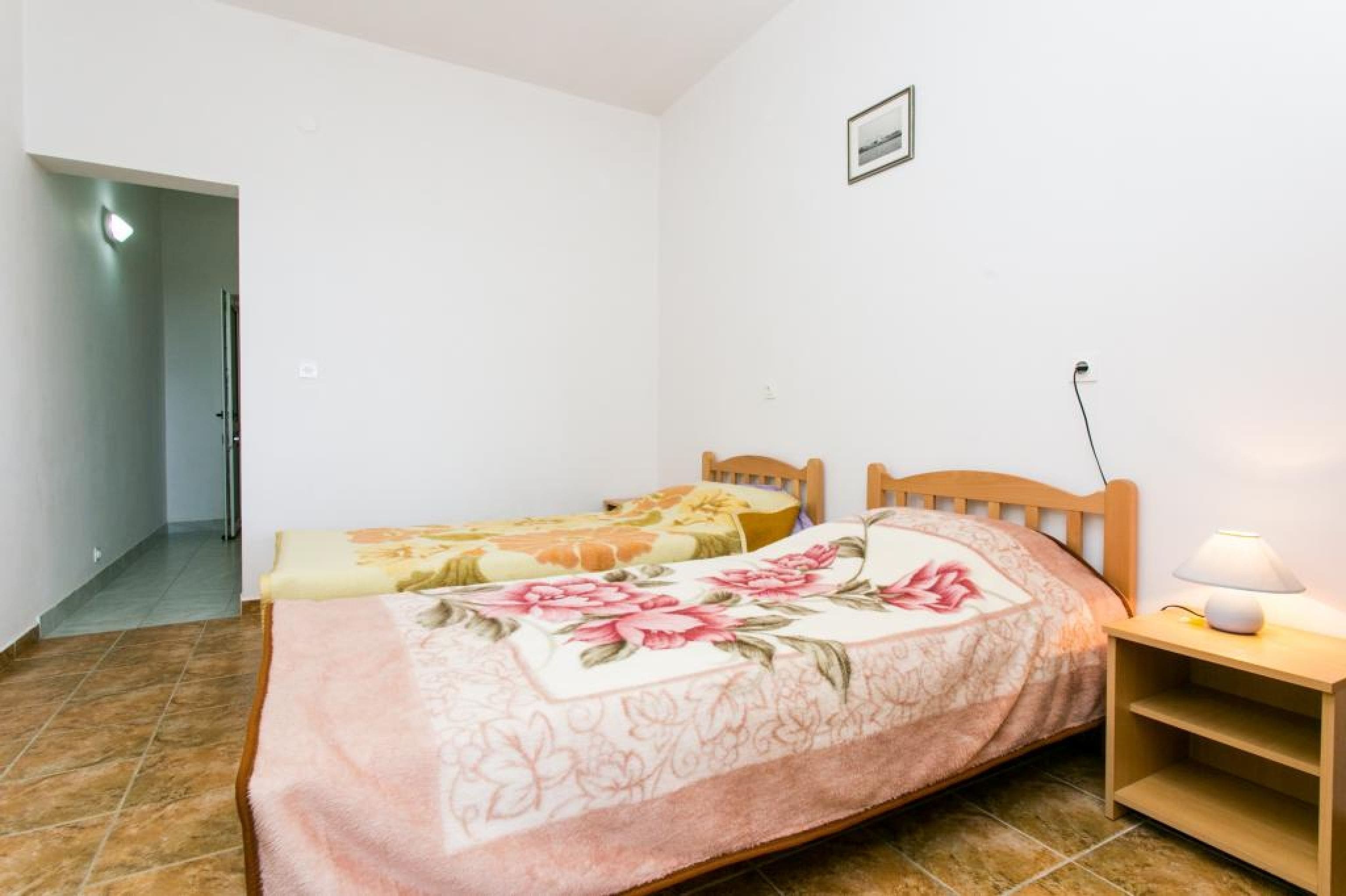 A bedroom with two beds, a nightstand with a lamp, and a door leading to another room.