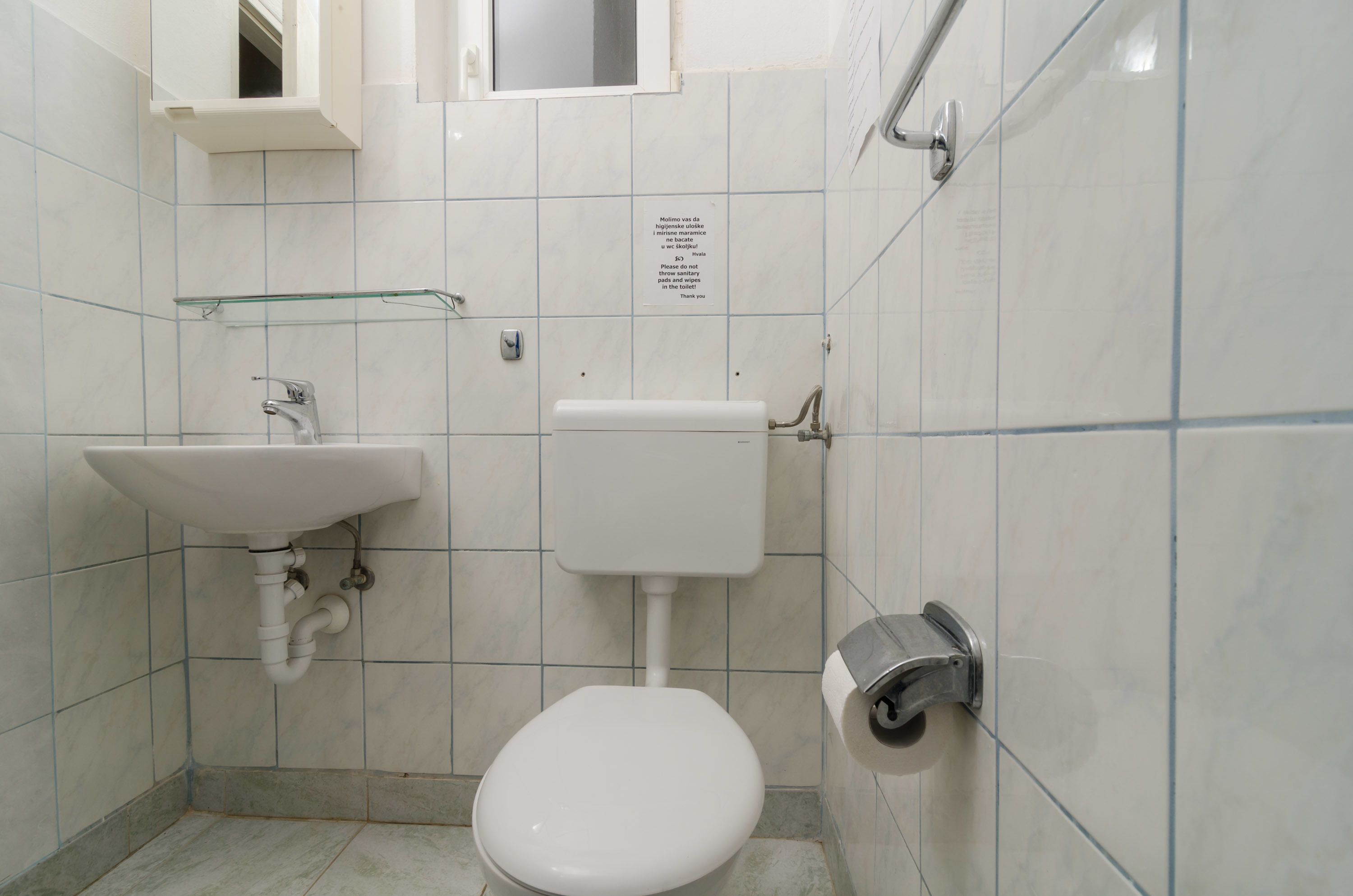 A small, clean bathroom with a toilet, sink, and a glass shelf.