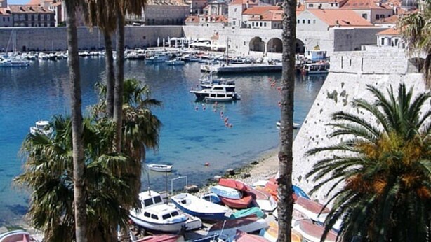 Une ville côtière dotée de bâtiments historiques, d’un port où sont amarrés des bateaux et d’imposantes fortifications.