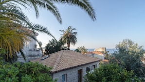 A stone building with a tiled roof, surrounded by lush greenery and palm trees. - Rooms Lydia - Adults Only (Dubrovnik)
