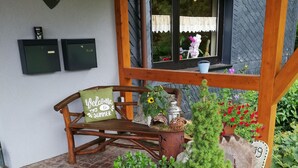 Een houten bank met een bordje 'Welcome to Summer', een bloempot en een stenen muur met een raam.