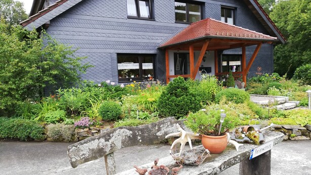 Een huis met een tuin ervoor, een bank met planten en een bord, en een overdekte veranda.