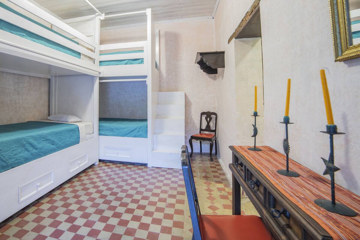 Quarto com beliches, uma cadeira, uma mesa e um espelho.