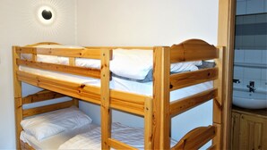 A bunk bed with a wooden frame and white bedding, a round wall light, and a bathroom with a sink and cabinet.