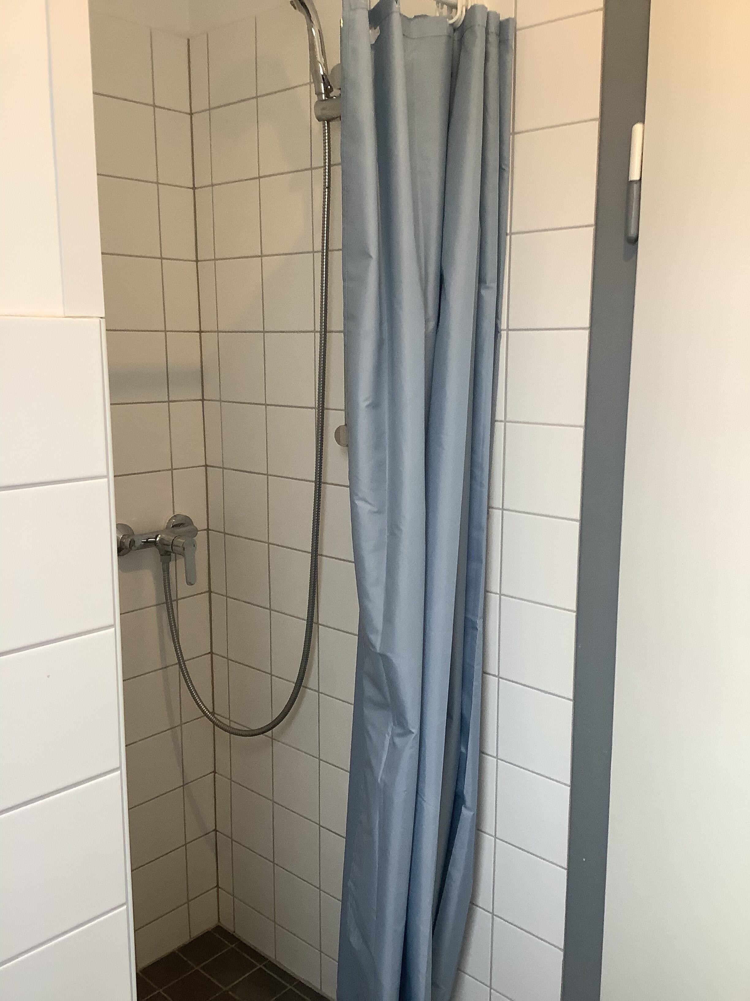 Un espacio de ducha con cortina azul, paredes de azulejos blancos y un cabezal de ducha.