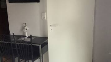 Une pièce comprenant un lit, un bureau et une chaise. On y trouve une porte blanche et un téléviseur fixé au mur.