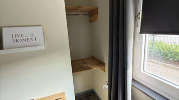 A small room with a wooden shelf, a sign that says 'LIVE in the MOMENT', and a window with a view of greenery outside.