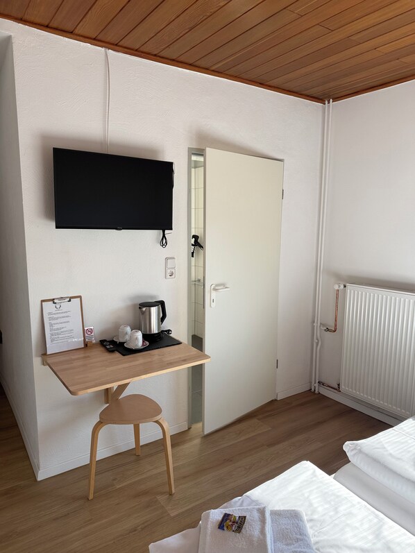Una habitación con un escritorio de madera, una silla, una cama, un radiador y un televisor fijado en la pared.