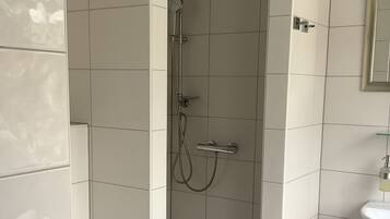 Een moderne badkamer met witte tegels, een douche, toilet en wastafel.