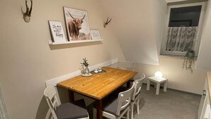 A dining area with a wooden table and white chairs, a small side table with a lamp, and wall-mounted decor including a framed picture and antlers. - Budgethotel Stadtbett Wolfsburg (Wolfsburg)