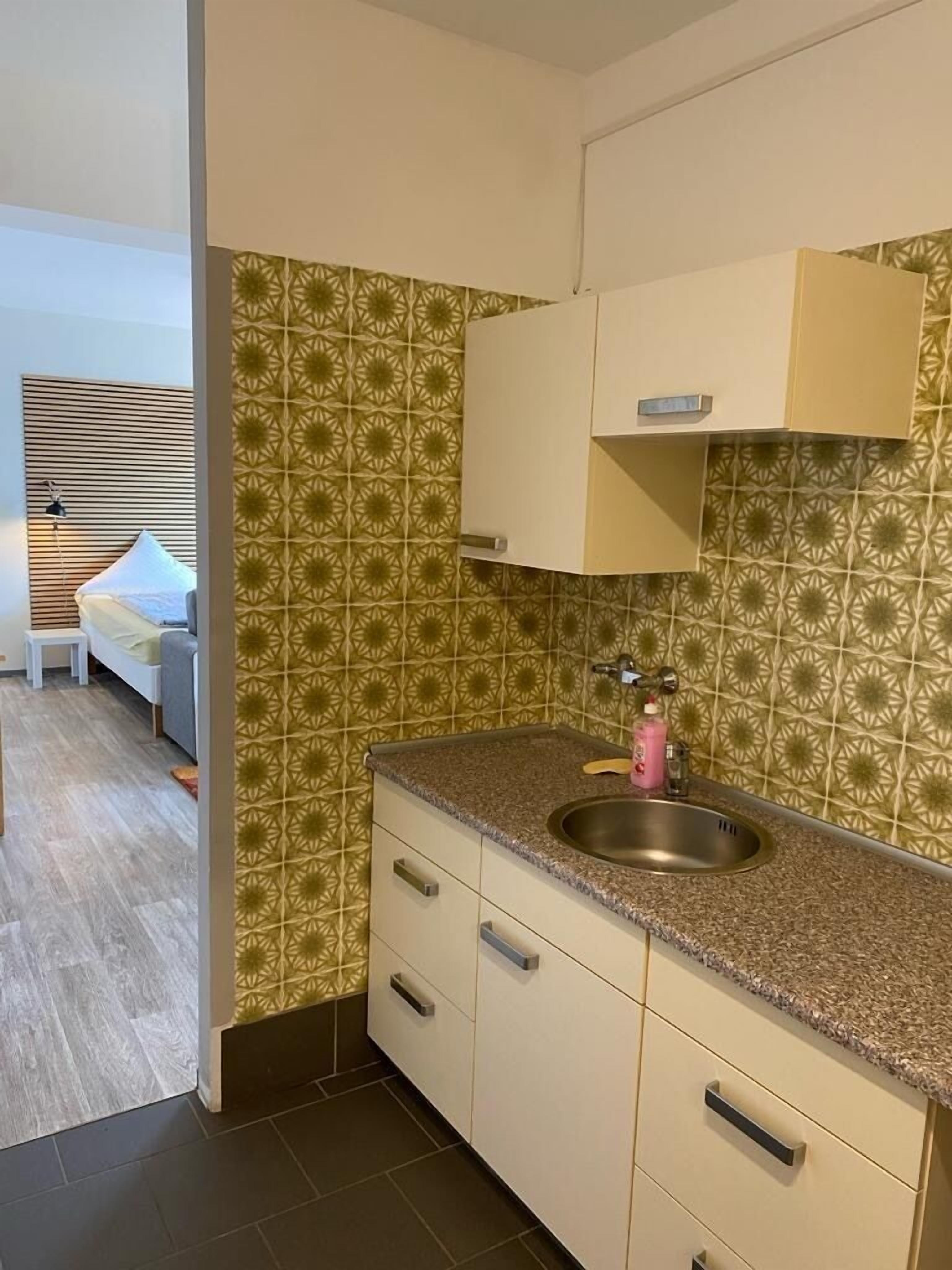 A compact kitchen with a granite countertop, a stainless steel sink, and a patterned backsplash.