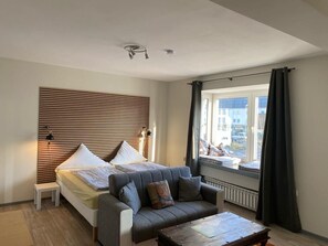 Un dormitorio moderno con una cama, un sofá, una mesita y un ventanal con cortinas.