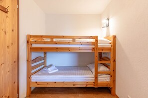 Un lit superposé avec une structure en bois et une literie blanche, un luminaire fixé au mur et une porte dotée d’une poignée.