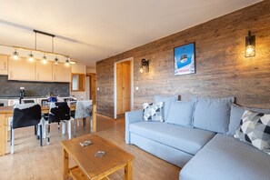 Un salon moderne avec un plancher en bois, un canapé et une table basse. Il y a également un coin cuisine avec des armoires en bois et une table à manger avec des chaises.