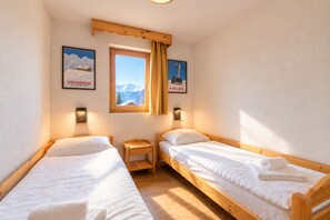 Een kleine, gezellige kamer met twee houten bedden, een raam met uitzicht op bergen en twee wandlampen.