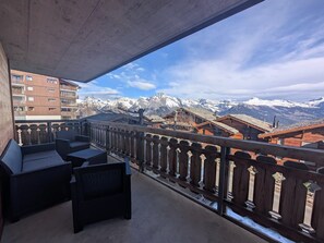 Een balkon met rieten meubilair met uitzicht op een berglandschap en traditionele gebouwen.