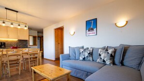 A modern living room with a grey sofa, wooden dining table, and chairs. There is a kitchen area with wooden cabinets and a coffee machine. - Pracondu 1 101 - OUTDOOR & FUN  apartment 8 pers (Haute-Nendaz)