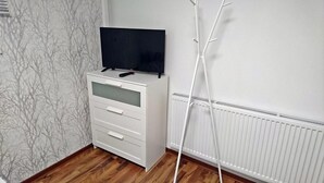 A white cabinet with a flat-screen TV on top, a radiator, and a tree-patterned wallpaper. - City Apartment S & W (Hamburg)