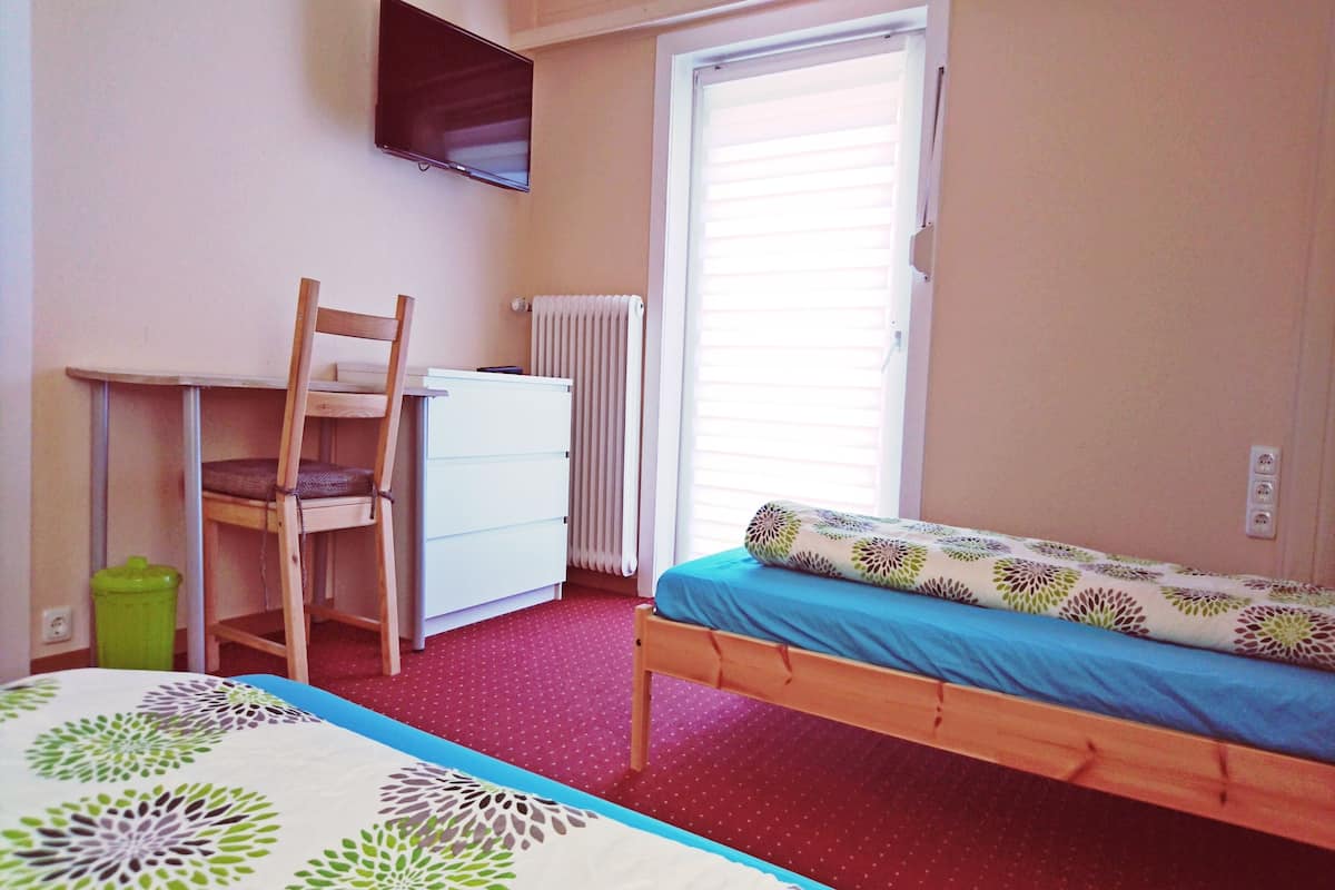 Un dormitorio con una cama nido, un escritorio con silla, un radiador y una televisión en la pared.
