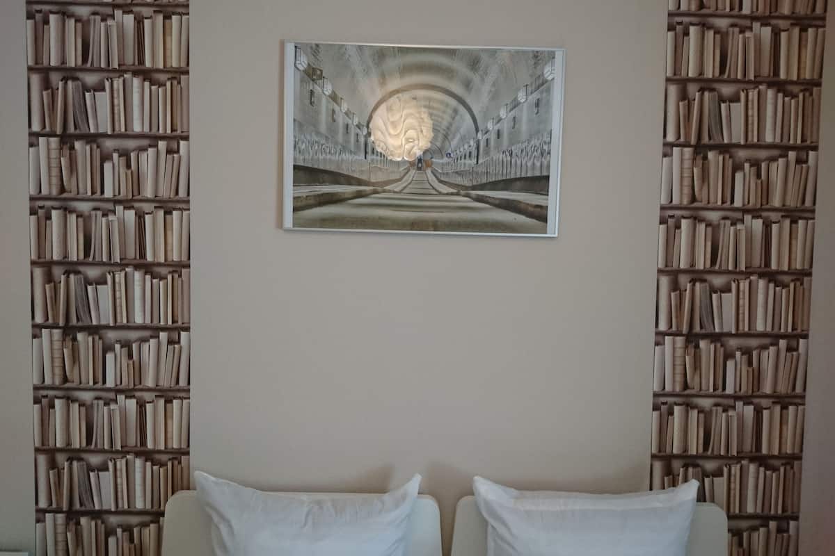 Una habitación con una gran estantería a ambos lados, un cuadro en la pared y dos camas blancas.