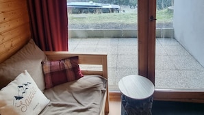 A room with a bed, a small round table, and a view of a forested area through a sliding glass door.