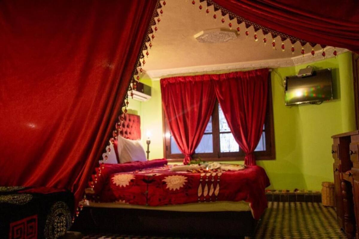 A room with a bed, red curtains, a television on the wall, and a patterned rug.