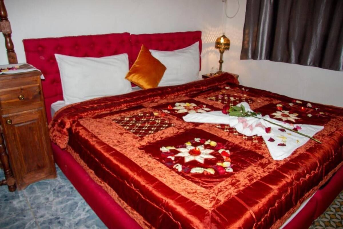 A neatly made bed with a red velvet bedspread, white pillows, and a decorative centerpiece.