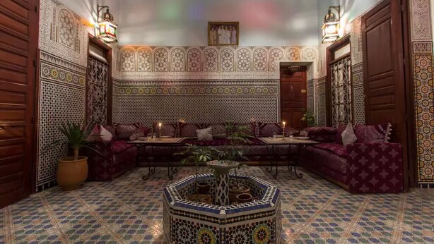 A Moroccan-style lounge with patterned tile flooring, a central coffee table, and a sofa set. - Riad Baba (Fes)