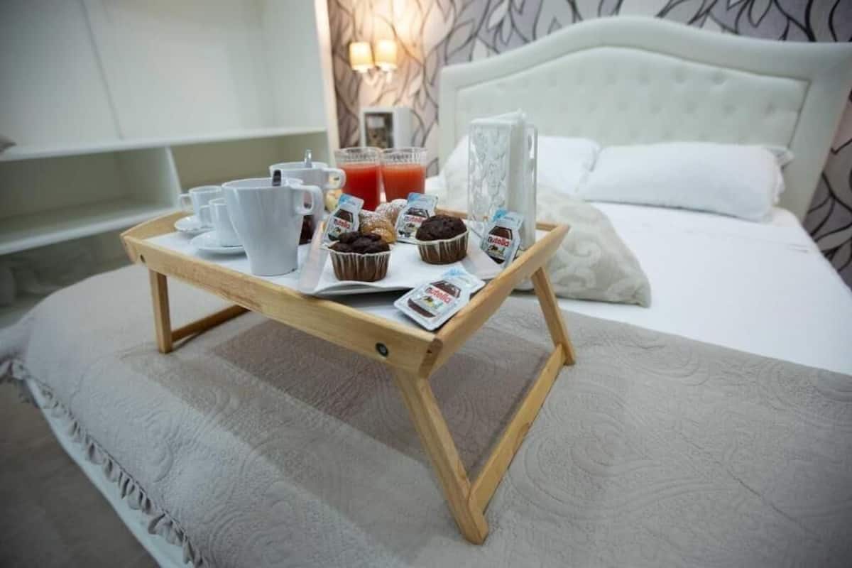 A breakfast tray with cups, muffins, and juice on a bed with a white headboard and pillows.