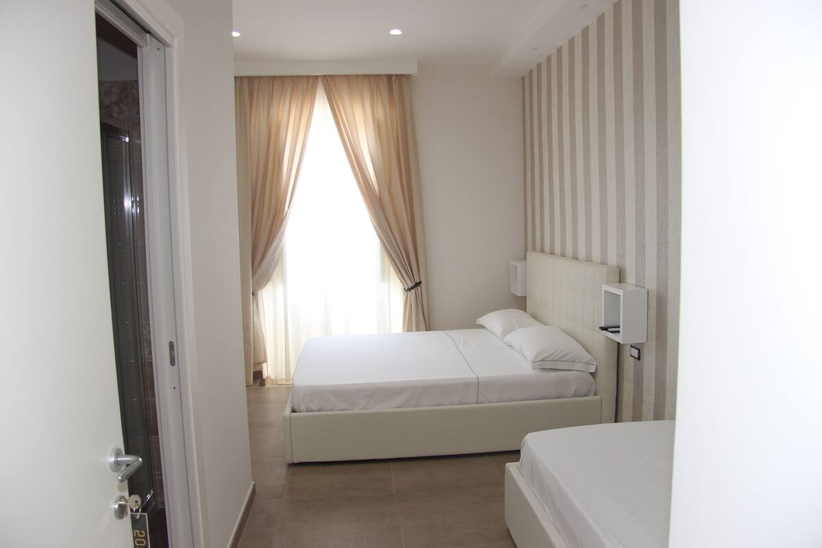 A bedroom with a bed, a bedside table, and a window with curtains.