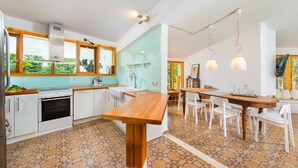 A modern kitchen with a wooden table, white cabinets, and a large window overlooking greenery. - Villa Ixia (Rhodes)