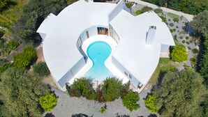 A modern, circular building with a central swimming pool, surrounded by lush greenery. - Villa Ixia (Rhodes)
