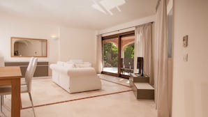 A modern living room with a white sofa, a dining table with chairs, and a large window with curtains. - Villa Pevero Hills 4 (Arzachena)