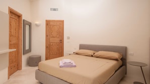 A bedroom with a bed, a bedside table, a round table, and two wooden doors. - Villa Pevero Hills 4 (Arzachena)