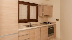 A kitchen with wooden cabinets, a stainless steel sink, a gas stove, and an oven. - Villa Pevero Hills 4 (Arzachena)