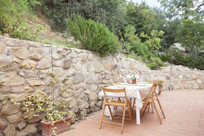 A stone wall with climbing plants, a table with chairs, and potted plants.