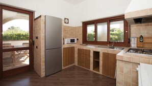 Una cocina con armarios de madera, un refrigerador, un microondas y una ventana con vistas a la vegetación.