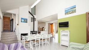 Una sala de estar moderna con comedor, una escalera y un televisor montado en una pared verde.
