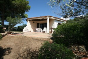 A white building with a tiled roof, a covered porch with chairs, and a stone wall. - Villa Scarabeo (Maracalagonis)