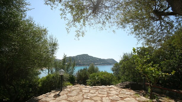 A stone pathway leading to a scenic view of a lake and hills. - Villa Scarabeo (Maracalagonis)