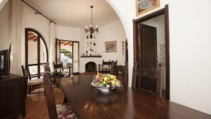 Un comedor con una mesa de madera, sillas, un frutero y una araña.