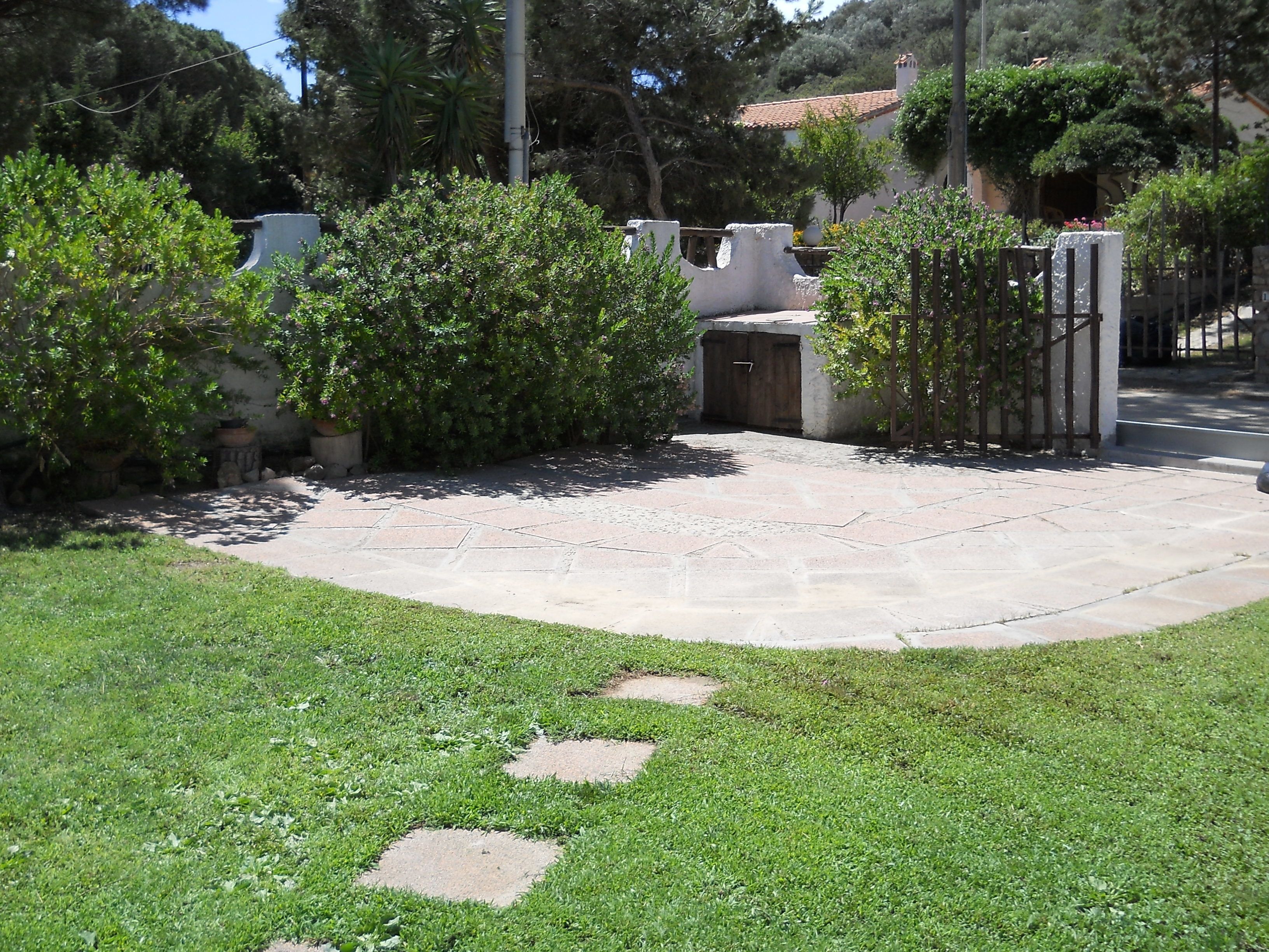 Un patio lastricato con un prato antistante e un muro di pietra con un cancello.