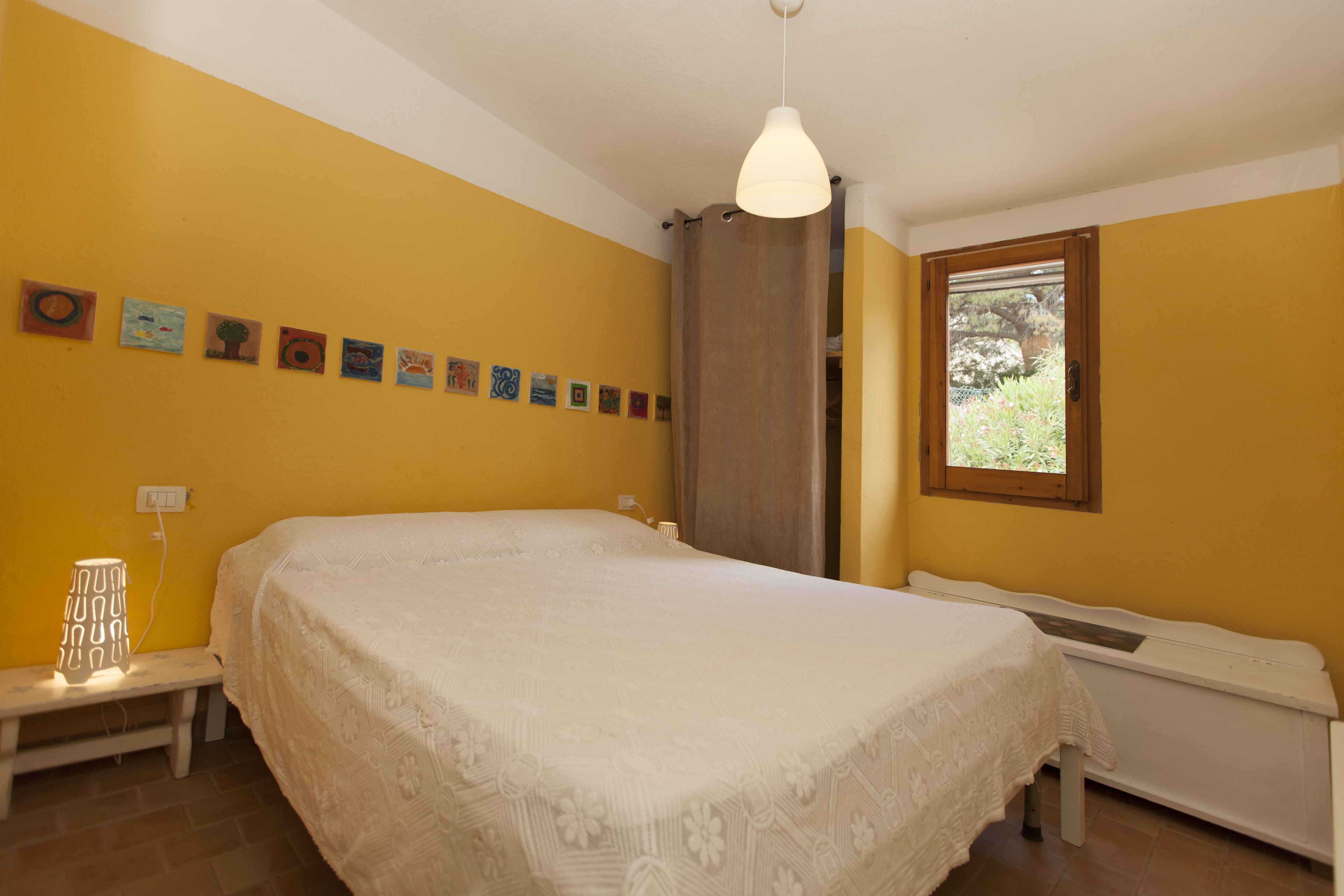 A bedroom with a large bed, a bench, a radiator, and a window.