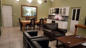 Un salon avec un canapé en cuir marron, une table basse en bois et un coin repas comprenant une table et des chaises en bois.