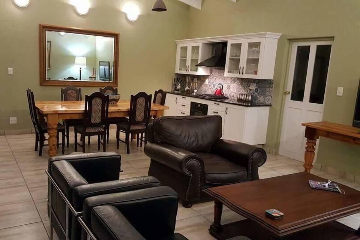 Una sala de estar con un sofá de cuero marrón, una mesa de centro de madera y un comedor con mesa y sillas de madera.