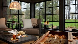 A cozy room with a large window, a sofa, a table with snacks and drinks, and a wooden board game.