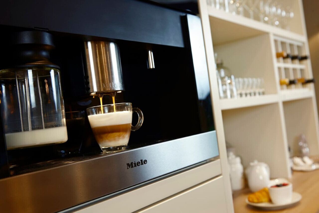 A coffee machine with a glass cup of coffee and a milk frother.