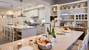 A modern kitchen with white cabinetry, a central island with a sink, and a breakfast setup including croissants and fruit.